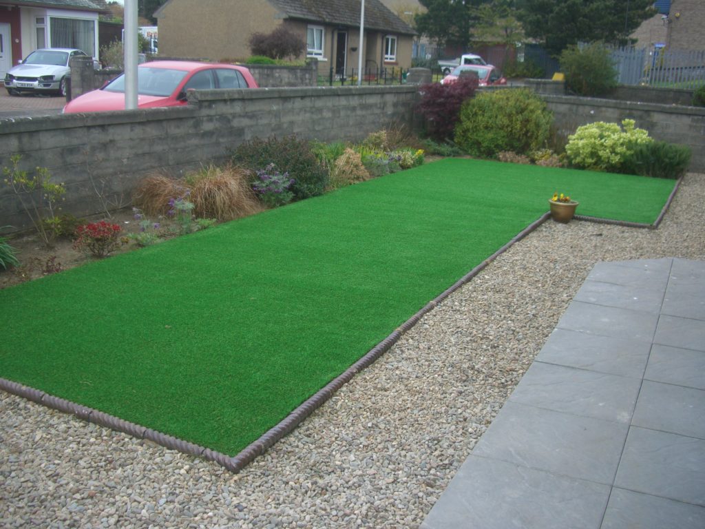 An artificial lawn surrounded by a border with stones and paving.