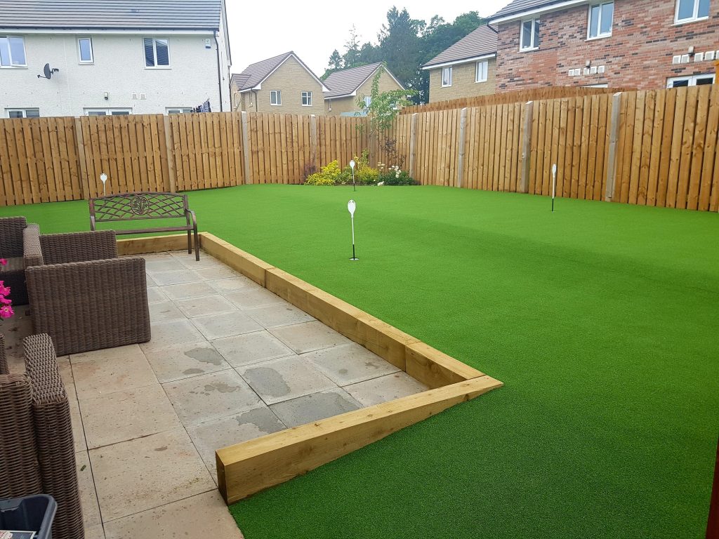 An artificial lawn in a garden with 4 putting holes for gold. Wooden fence around the garden.